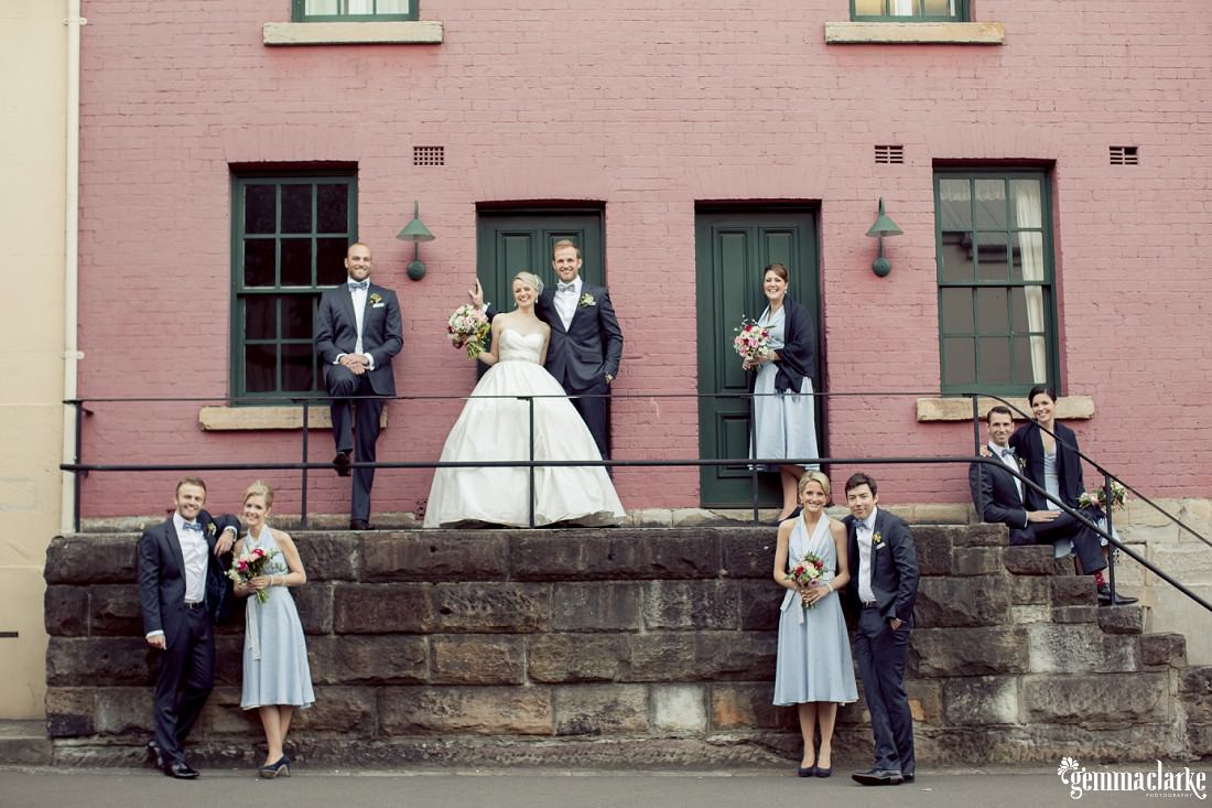 A bridal party posing around sandstone steps in front of a pink building - The Rocks Wedding