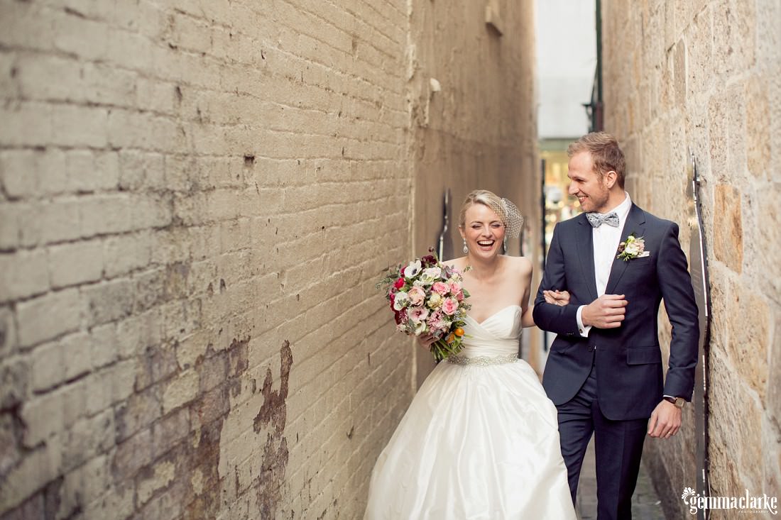 A bride and groom laughing as they walk arm in arm down an alley way - The Rocks Wedding