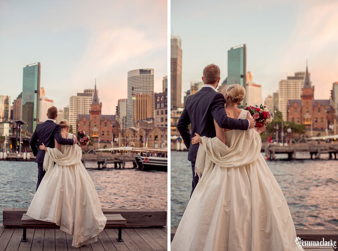 A bride and groom standing on a bench by the water with the Sydney skyline in the background - The Rocks Wedding