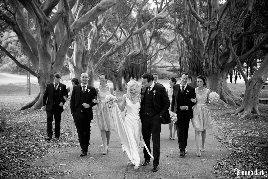 A bridal party walking two by two down a leafy path between some large trees - Eastern Suburbs Wedding