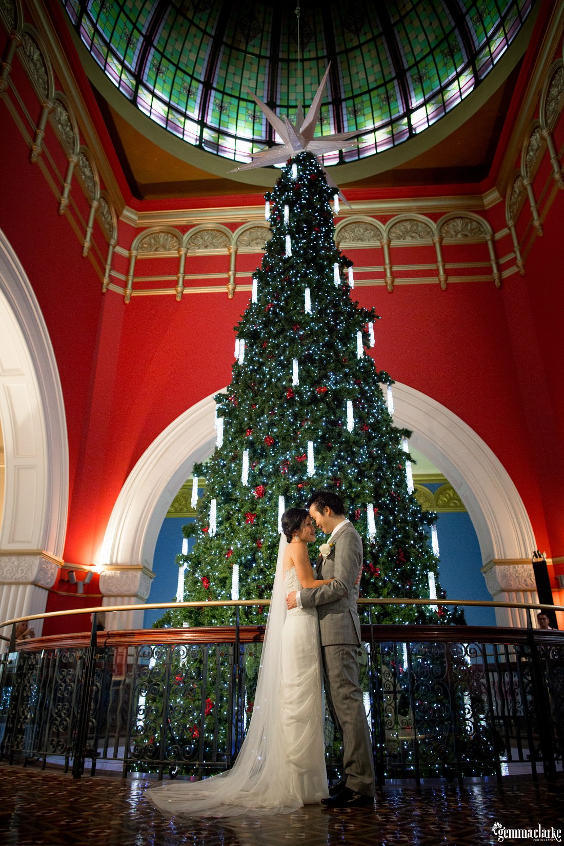 A bride and groom holding each other close in front of a large Christmas Tree in the Queen Victoria Building in Sydney - Secret Garden Wedding