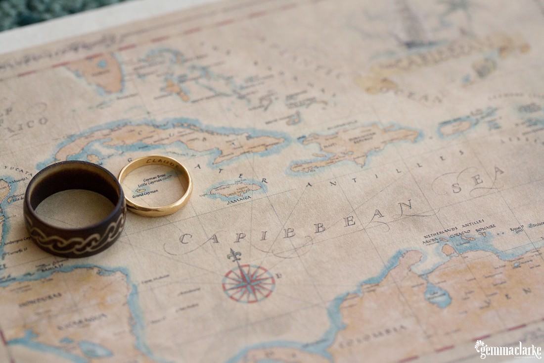 A gold ring and a tribal looking ring sitting on a map showing the caribbean sea for this caribbean elopment