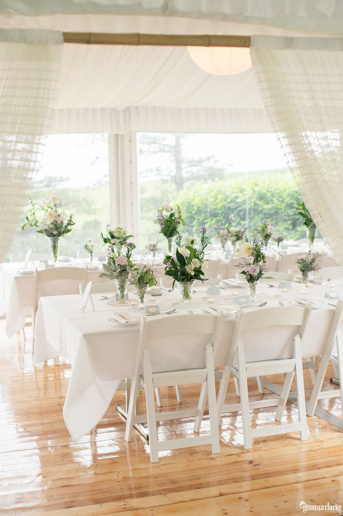 Sheer curtains framing the entrance to a marquee reception set with beautiful pastel flowers and white linen at this Bush Bank Wedding