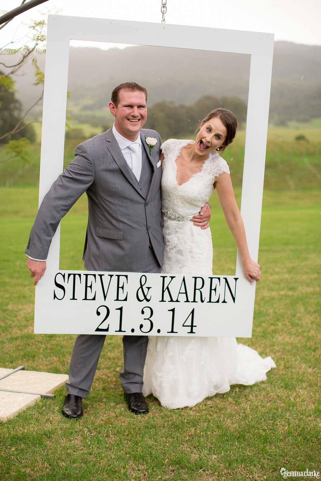 A bride and groom posing and smiling inside a large white "frame" - Silos Estate Wedding
