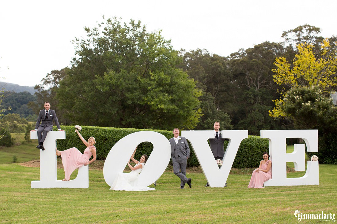 Large white letters spelling out the word LOVE standing on the lawn and the bridal party are draped across the different letters at this Silos Estate Wedding