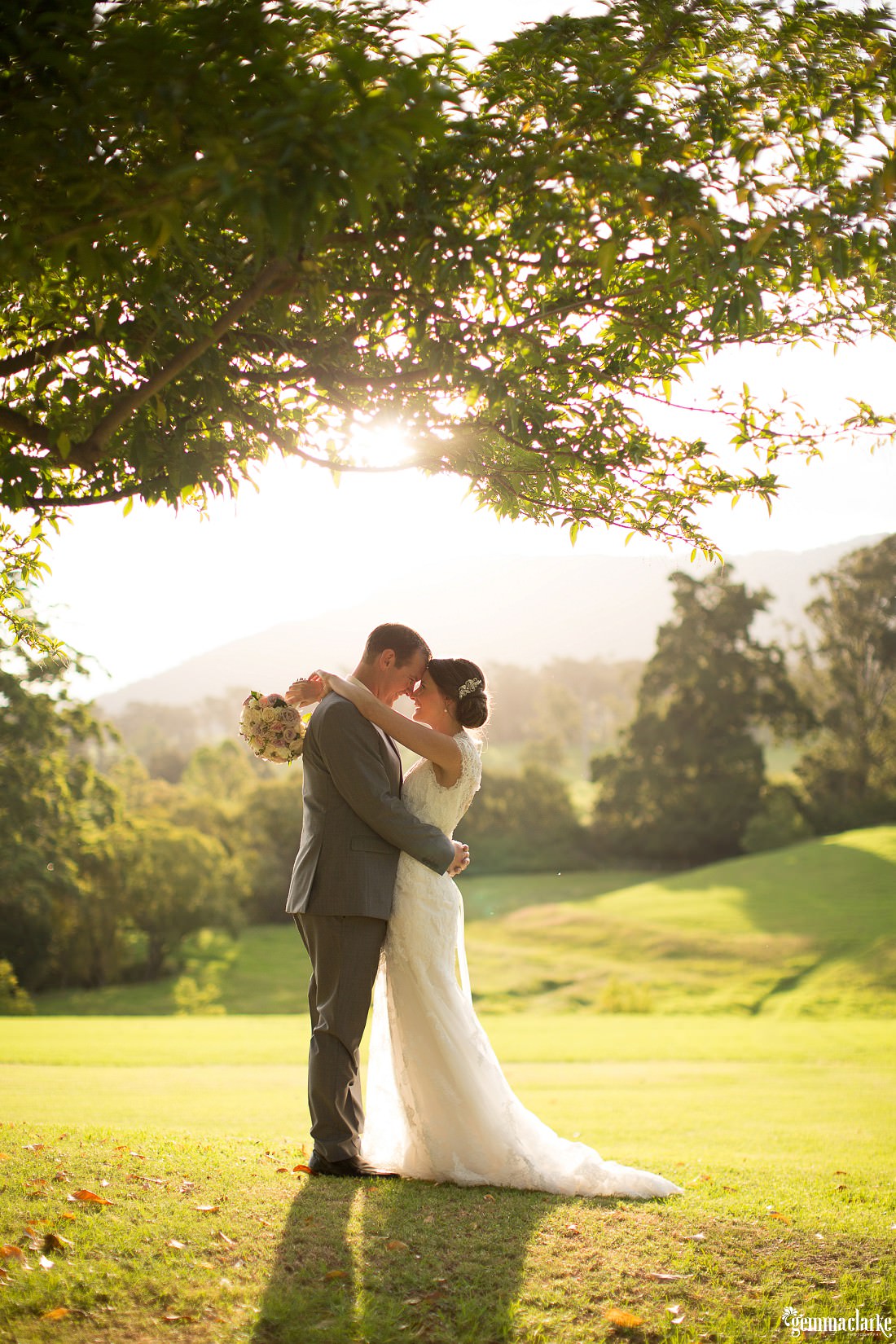 Magical sunset photos with the bride and groom hugging and looking into each other's eyes. There is an overhanging tree and the mountains in the background at this Silos Estate Wedding