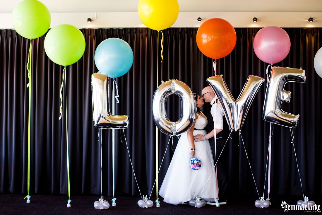 A bride and groom kissing while standing among balloons spelling out the word "love" – St Michael's Golf Club Wedding
