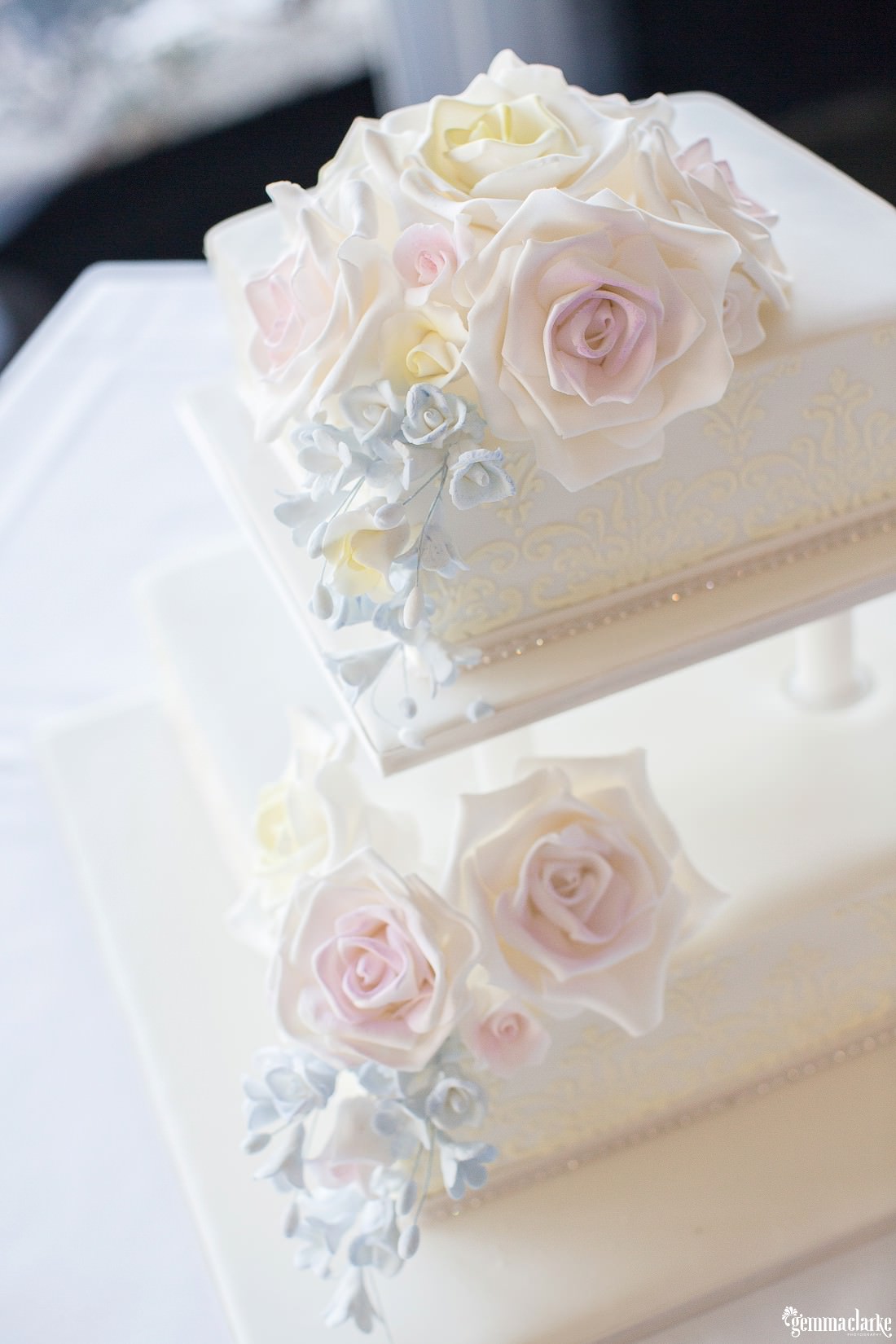 Two tiered white wedding cake with light coloured flower decorations - Dairy Precinct Wedding