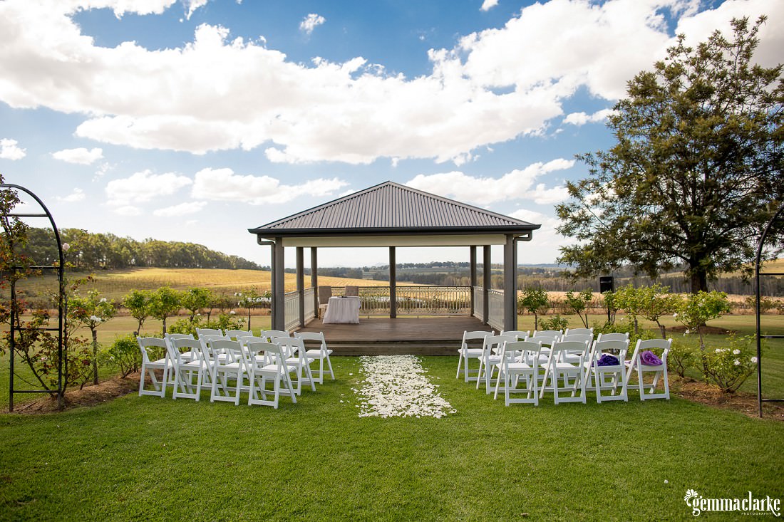 Outdoor wedding ceremony setup with a gazebo, white chairs, and white flower petal 'aisle' - Twine Restaurant Wedding