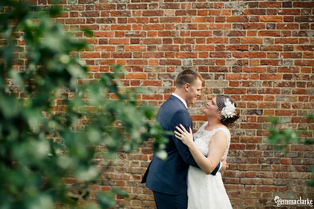 A smiling bride and groom embrace in front of a brick wall - Camden Wedding