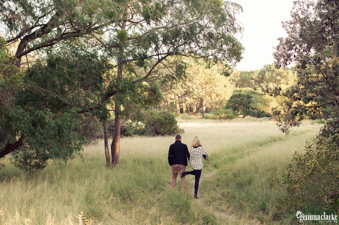 A woman playfully kicking a man in the butt as they walk along a trail through some long grass