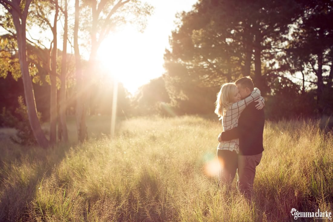 A man and woman embrace in the late afternoon sun in a field of long grass
