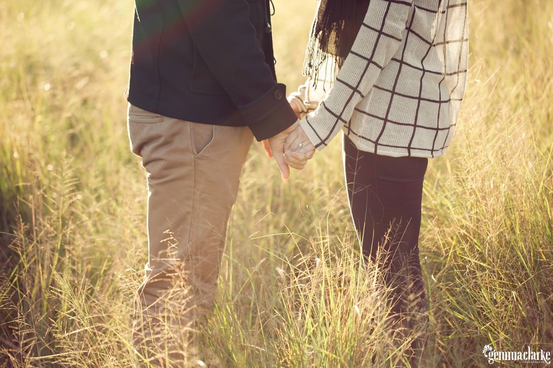 A closeup of a man and woman holding hands while standing in a field of long grass