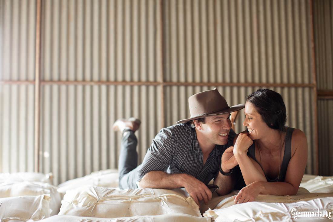 A man and woman laying on wool bales in a shed - Sunset Farm Portraits