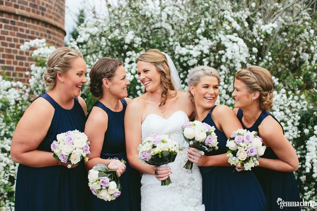 A bride and her bridesmaids standing close and smiling at each other