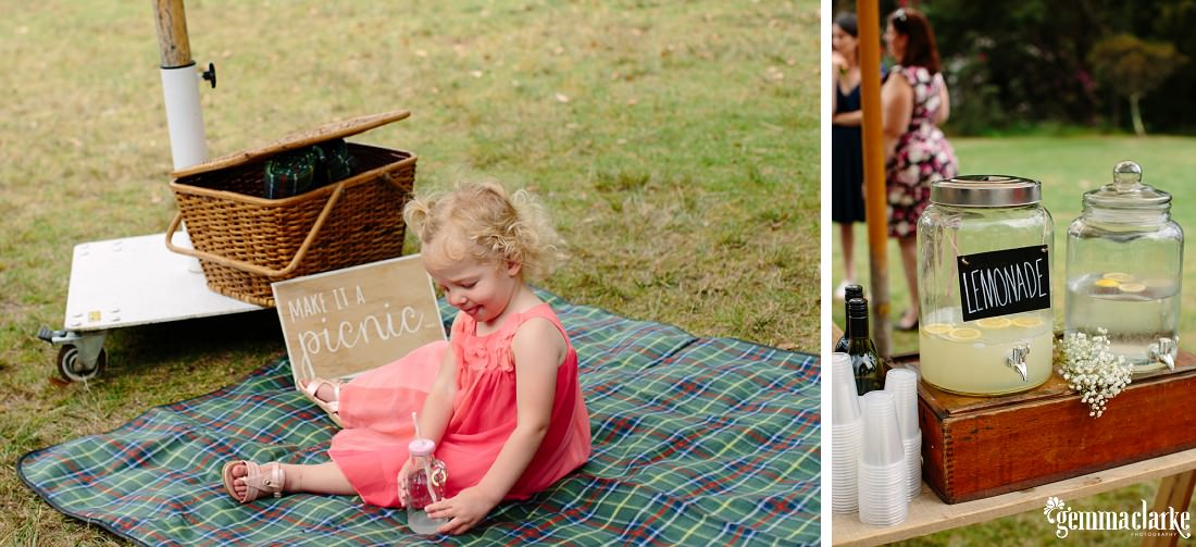 A young girl sitting on a picnic blanket and two large glass drink dispensers, one with a sign saying "Lemonade"