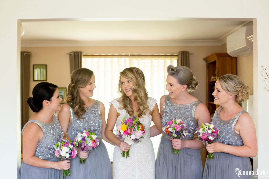 A bride and her four bridesmaids holding their bouquets and smiling at each other while standing in a wide doorway 