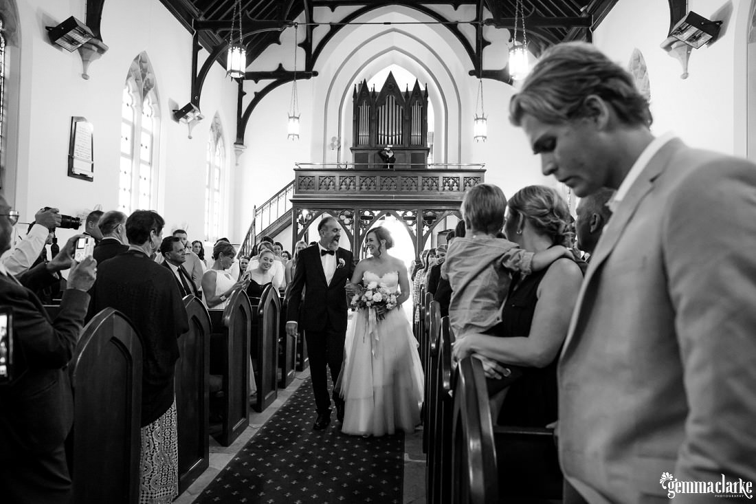 A bride and her father smile at each other as they walk together down the aisle of a church