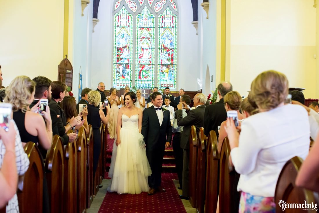A bride and groom are congratulated by wedding guests as they leave the church