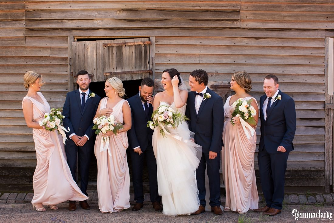 A smiling bridal party in front of a wooden farm building