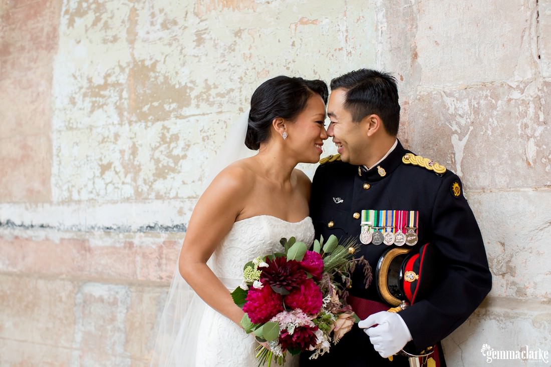 A bride and groom smiling and sharing an eskimo kiss against a stone wall