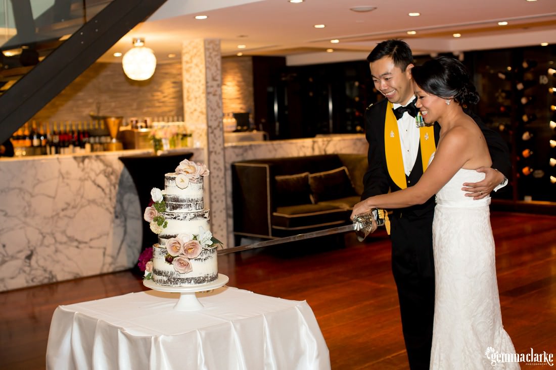 A bride and groom cut their wedding cake with the groom's ceremonial sword