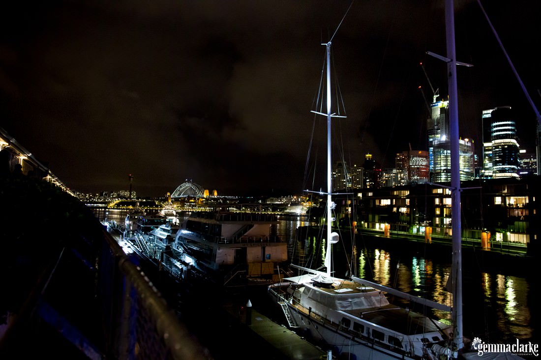 A night view of a yacht on the water with buildings and the Sydney Harbour Bridge in the background