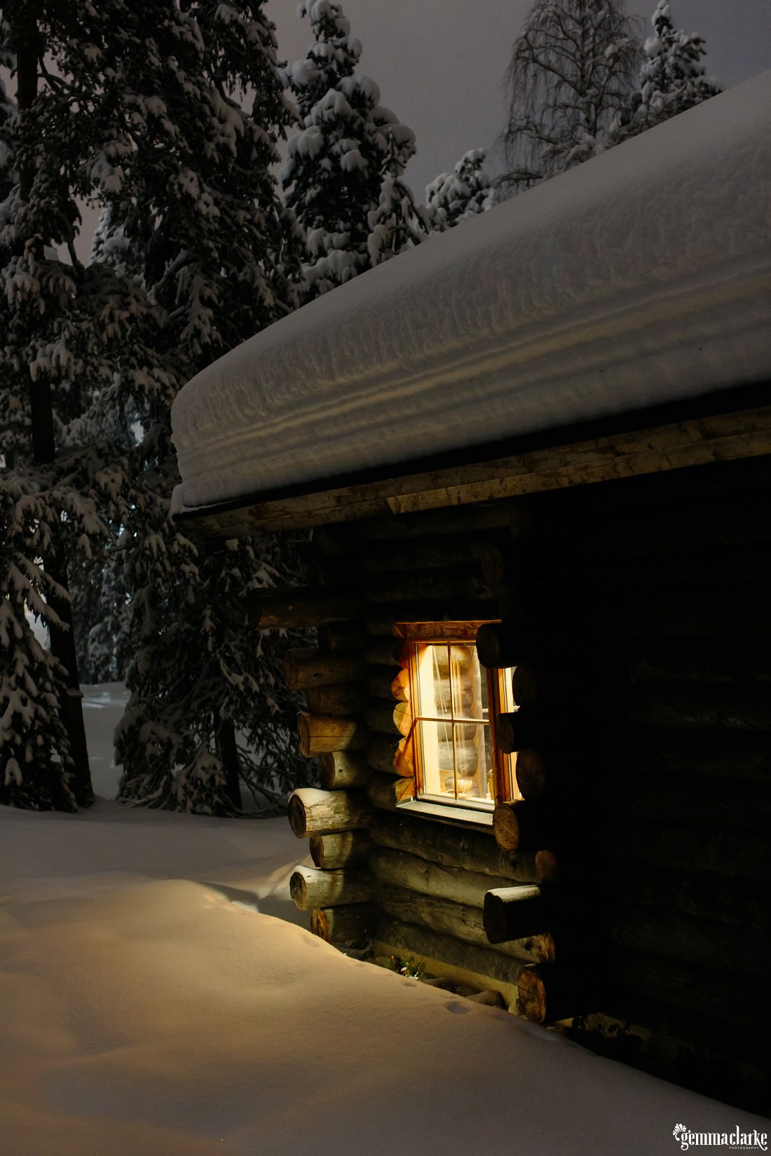 Light shining out from the window of a cabin with thick snow on the roof and ground
