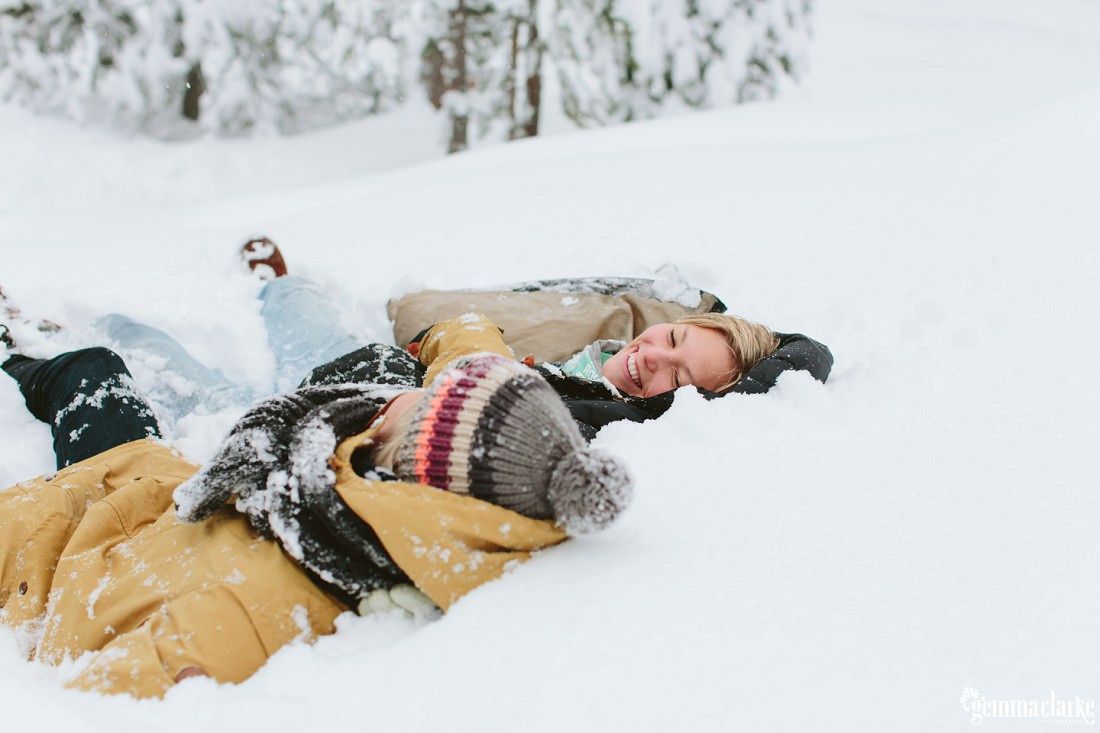 A couple smile at each other while laying in the snow