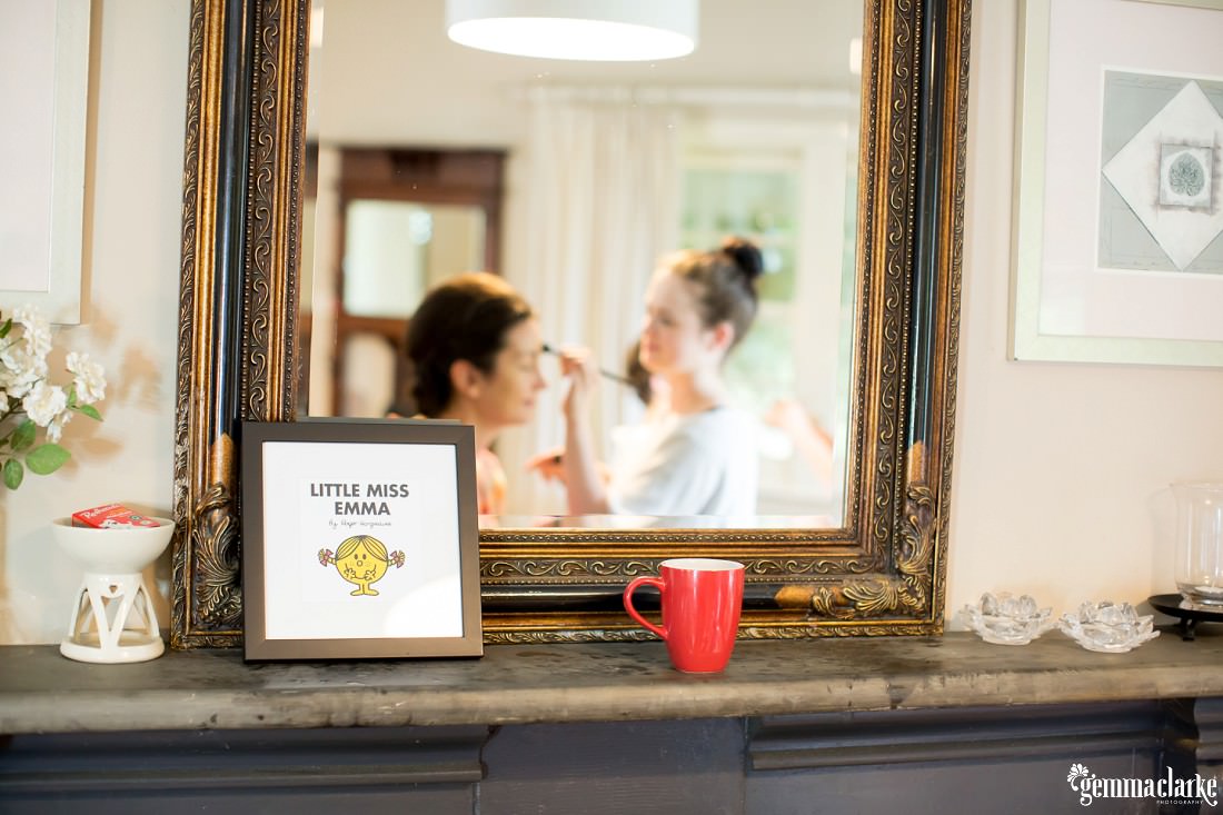 A Little Miss Emma book in front of a mirror showing a woman having her makeup done by a makeup artist