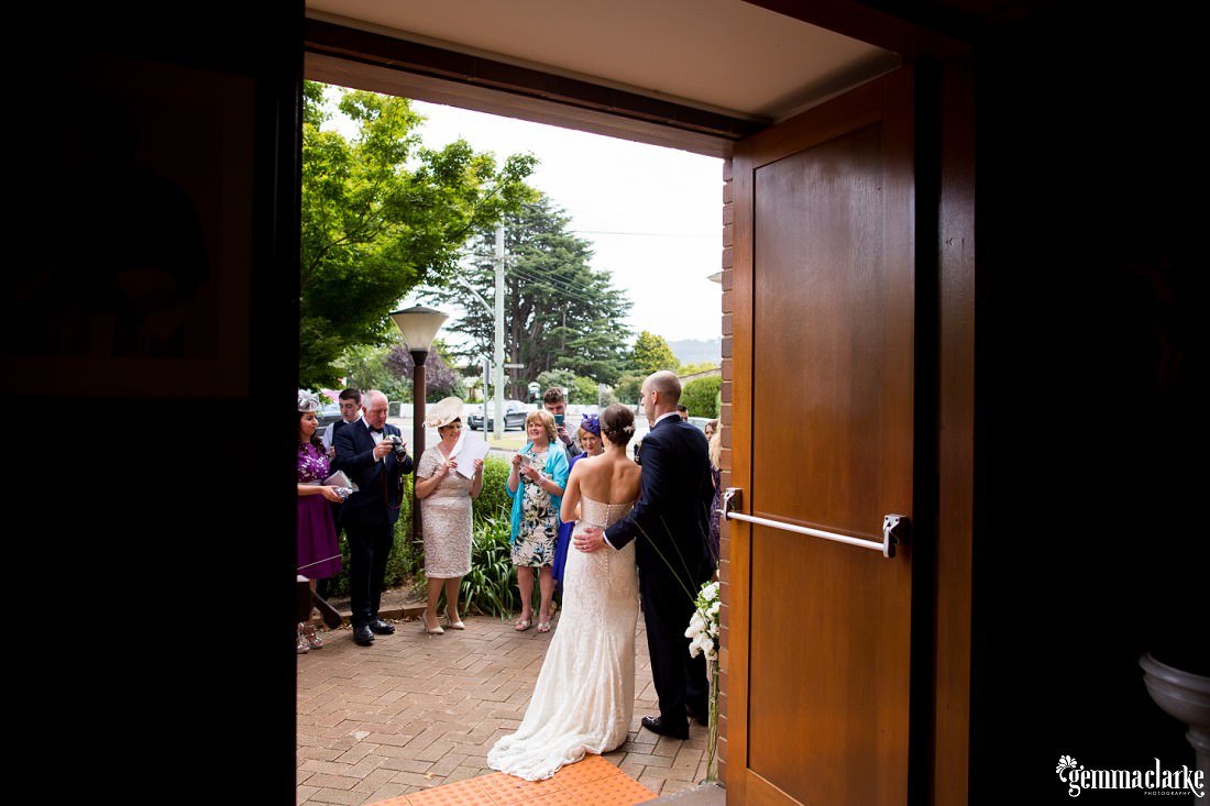 A bride and groom are greeted by their wedding guests outside the church after their ceremony