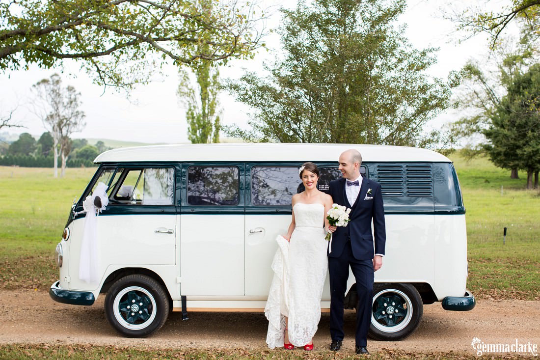 A bride and groom standing next to a Volkswagen Microbus on a dirt country road
