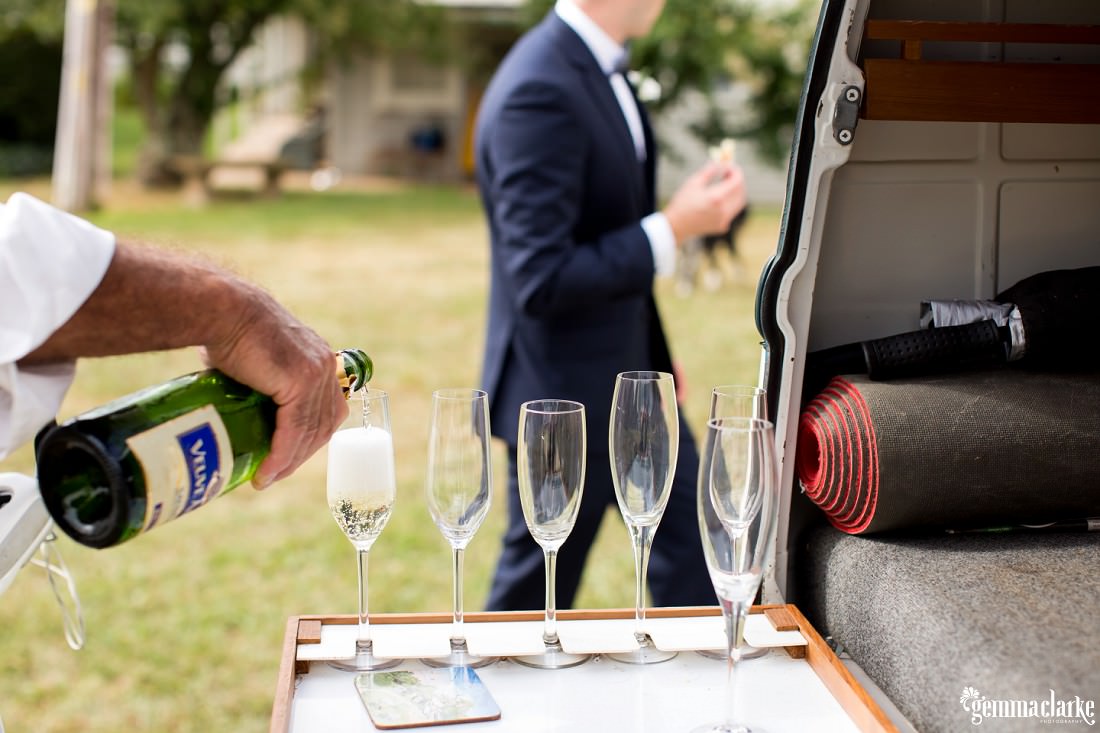 Champagne being poured into flutes while a groom walks past in the background
