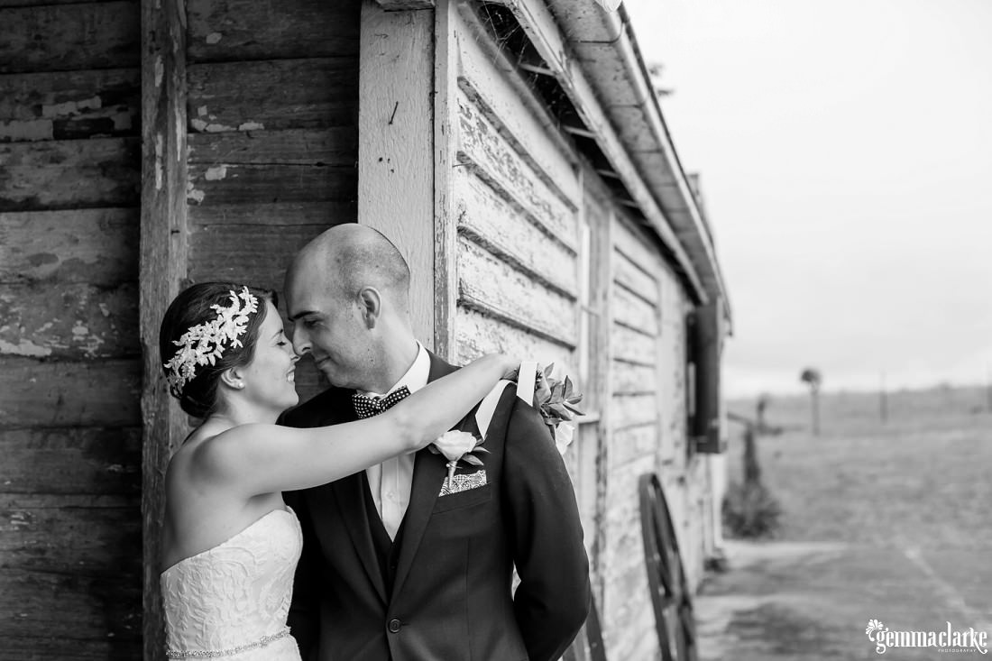 Eskimo kisses between a smiling bride and groom standing near a wooden country outbuilding