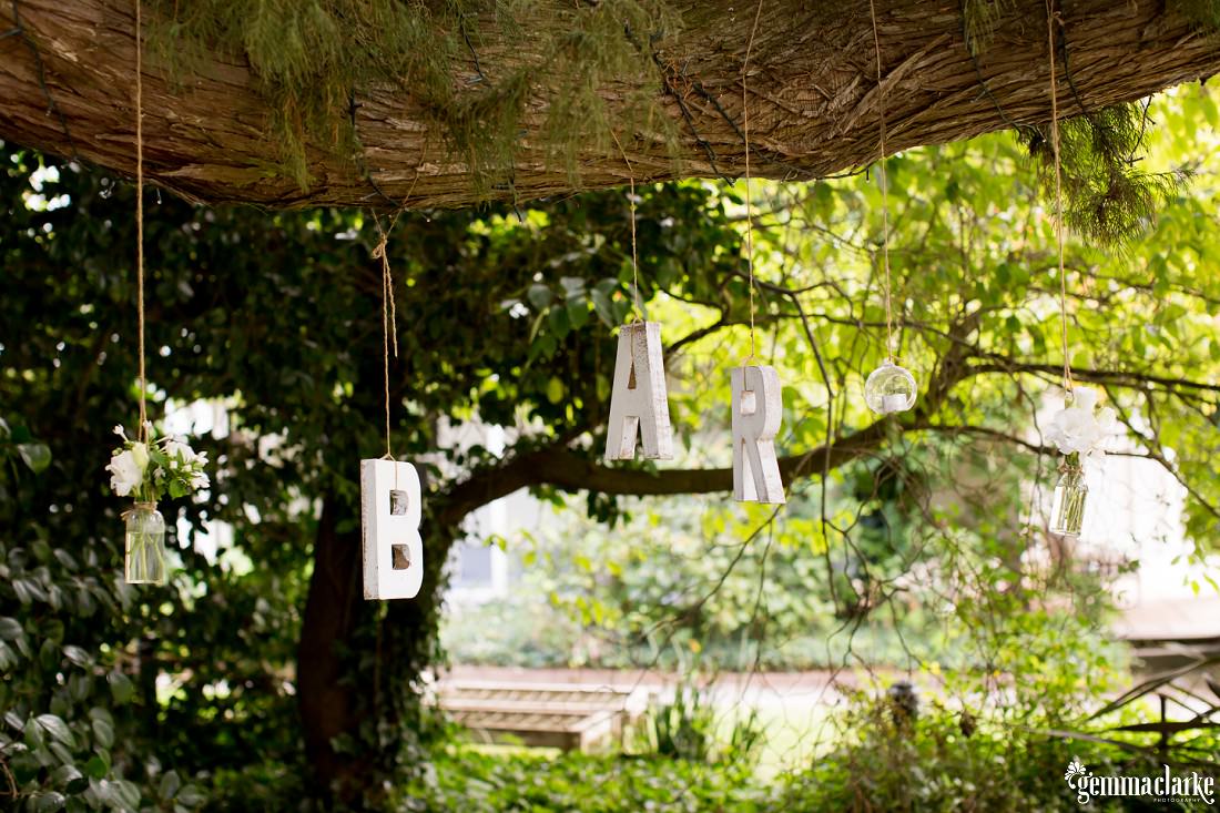 Flower jars and letters spelling out the word "bar" hanging from a tree branch