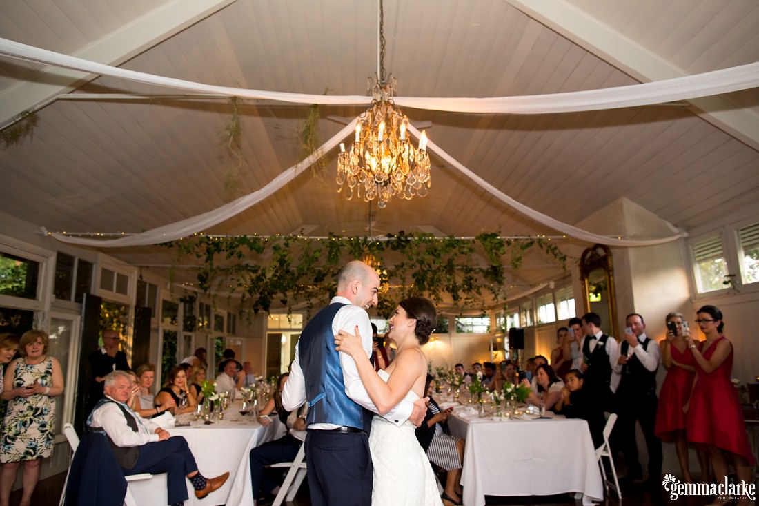 A bride and groom share their first dance as their wedding guests look on