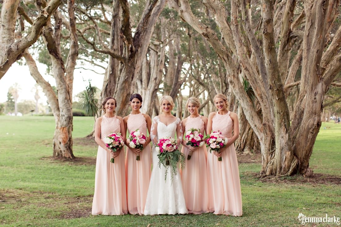 A bride and her bridesmaids standing together in front of some trees - Centennial Park Wedding