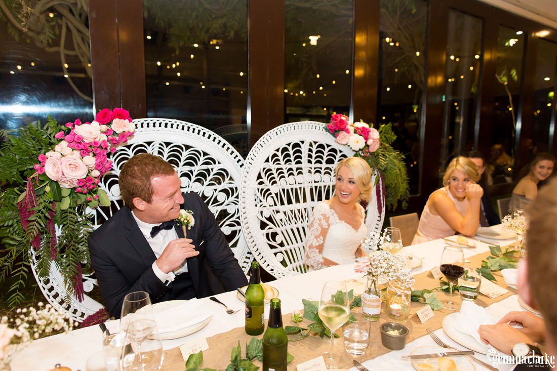 A bride and groom smile at each other while sat at the bridal table