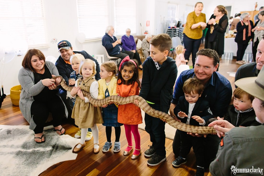 A lot of smiles as the small children, all in one line attempt to hold a large snake! at this animal themed birthday party