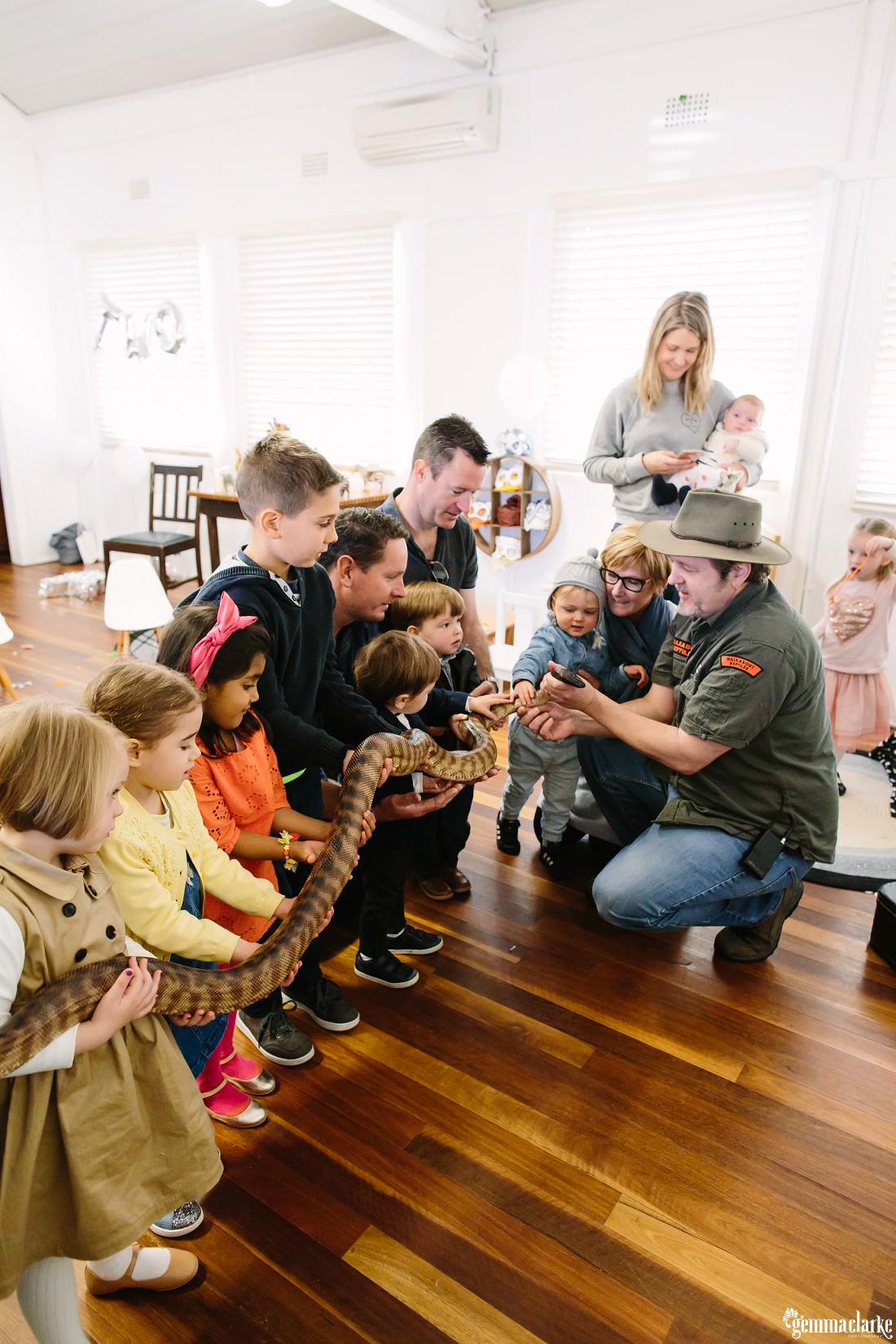 A row of small children all holding a large snake while the Ranger holds the head of the snake and yes, it is real!