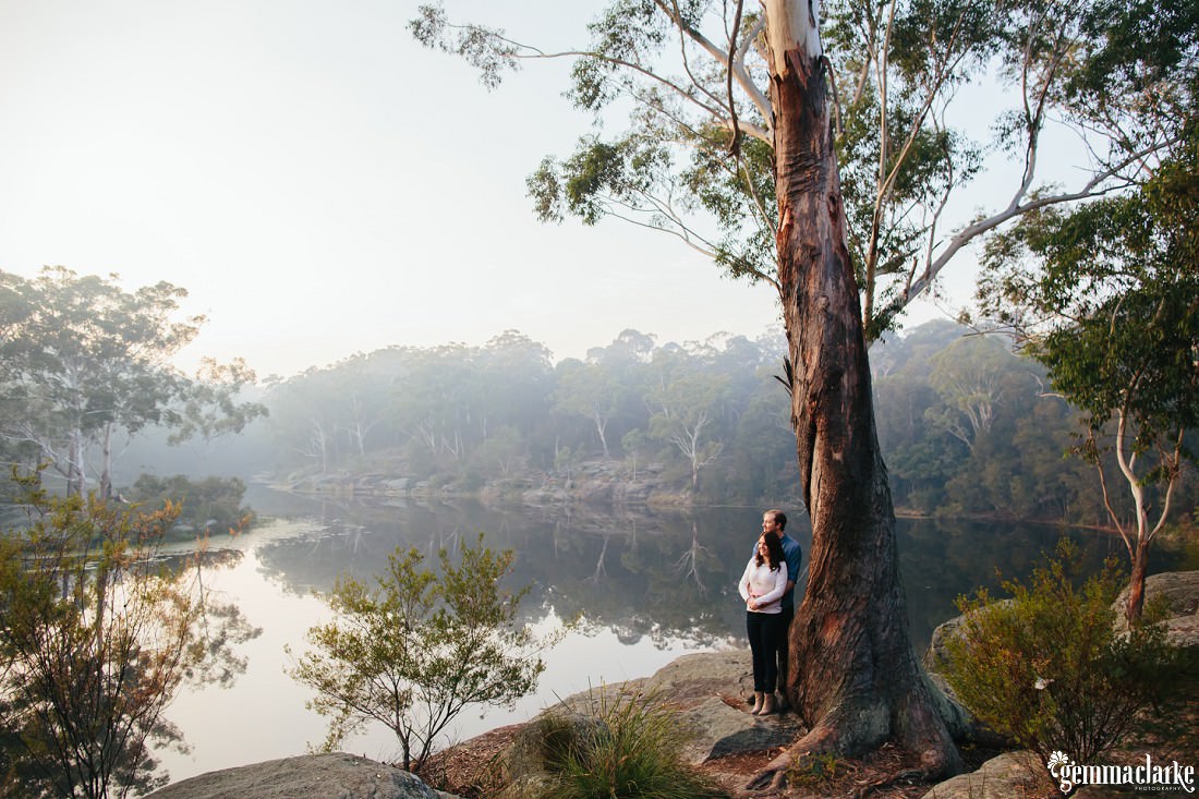 A large tree with couple standing by it cuddling and overlooking a large misty lake with reflections of the trees in the distance. This is my favourite photo at Lake Parramatta