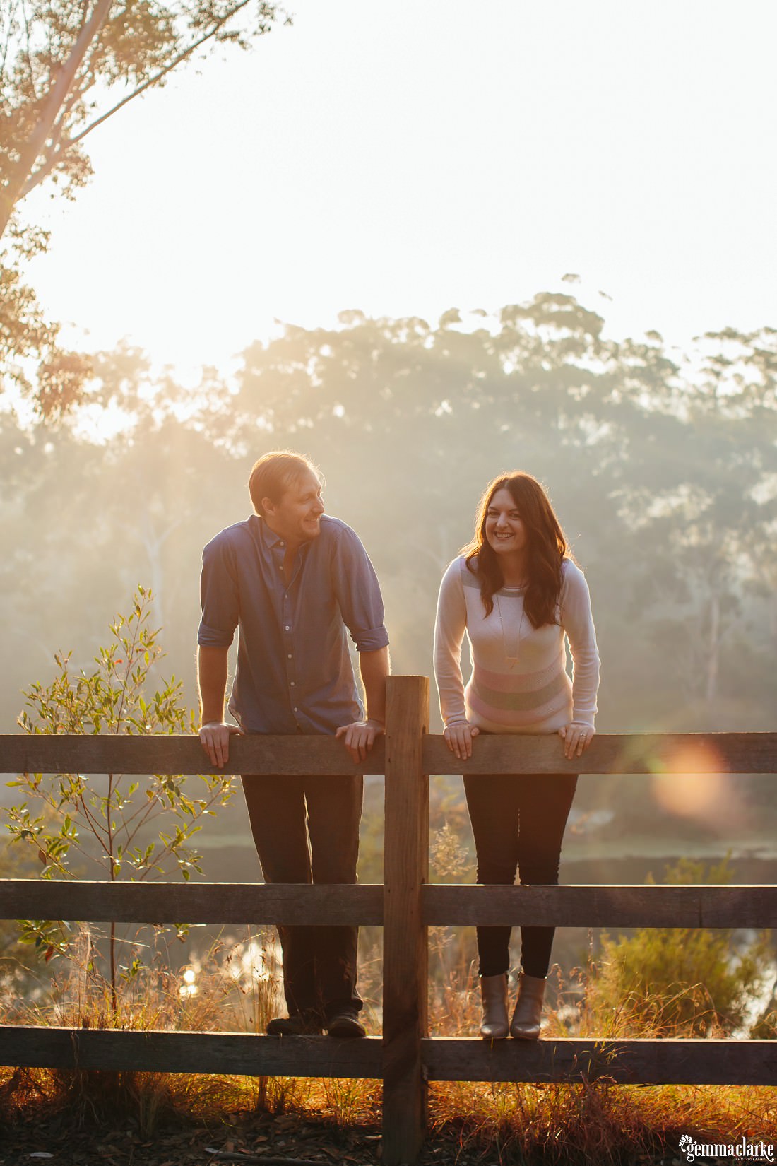 Couple standing on a wooden fence and hanging over while the sun streams over them at Lake Parramatta
