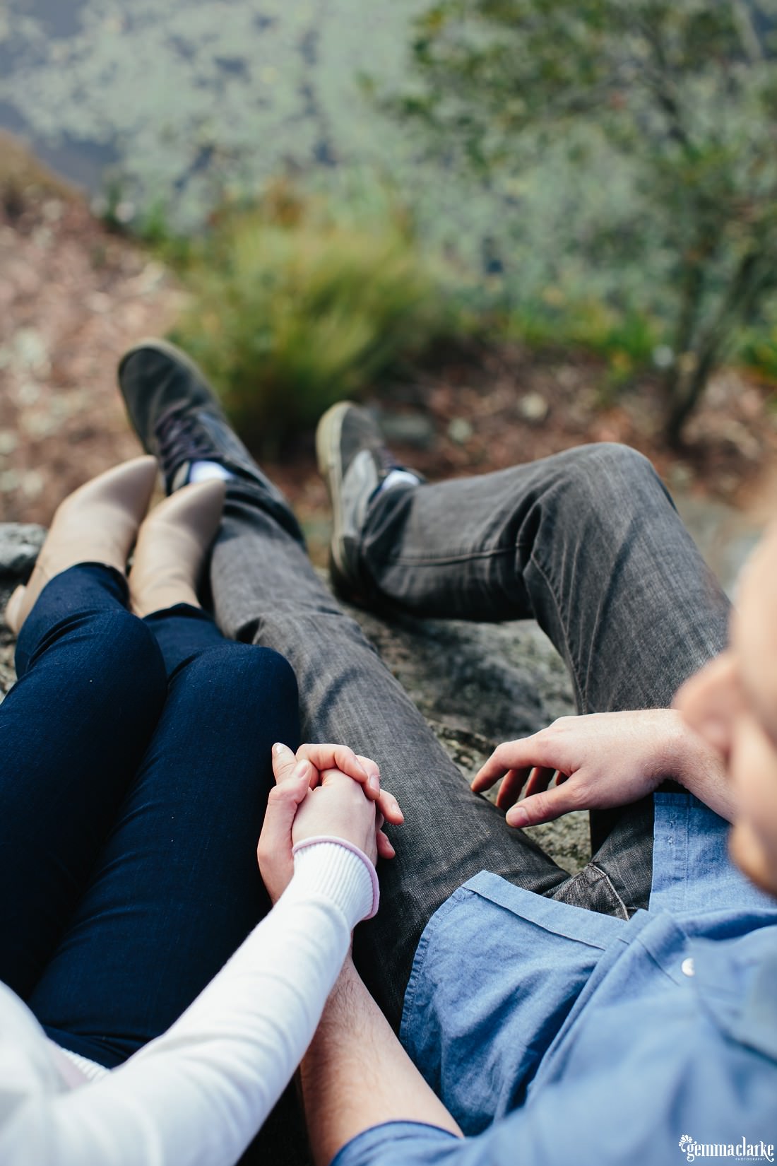 An overhead view of a couple holding hands whilst sitting on a rock at Lake Parramatta