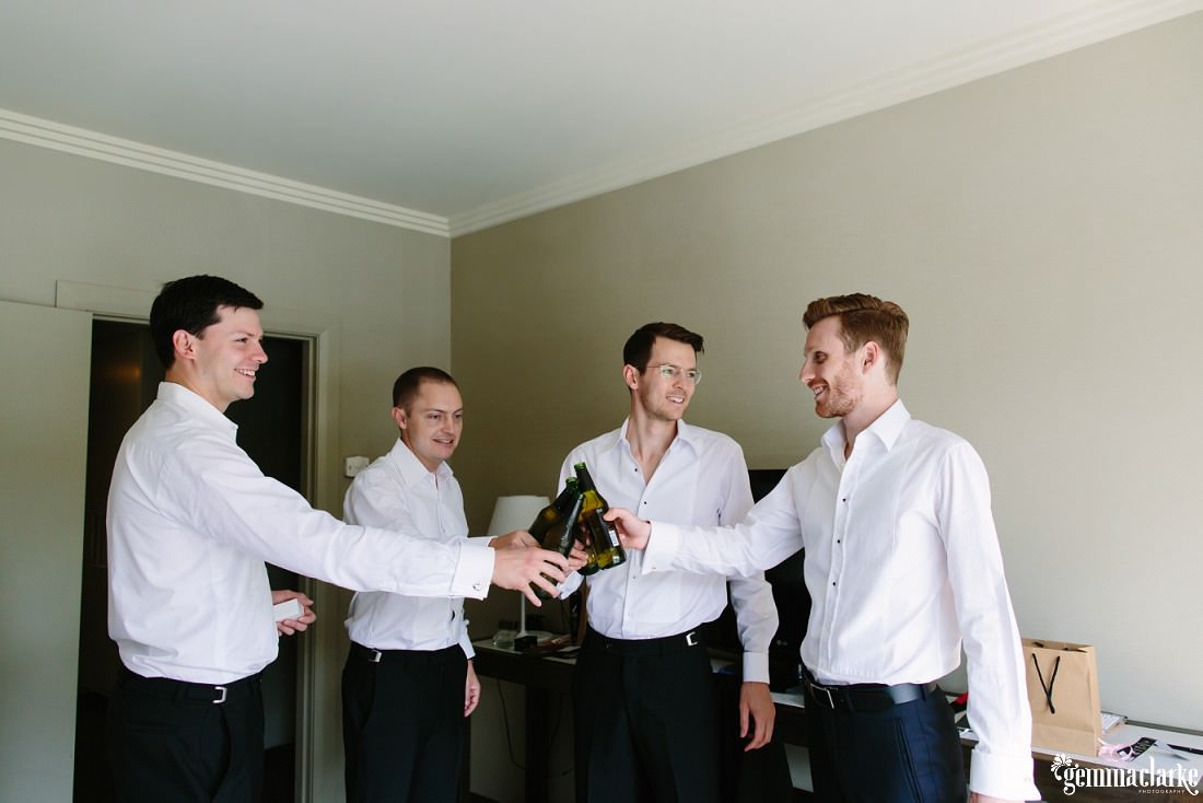 A groom and his groomsmen clink their beer bottles