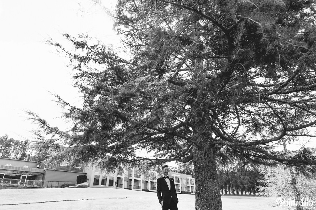 A groom smiling and standing under a large tree