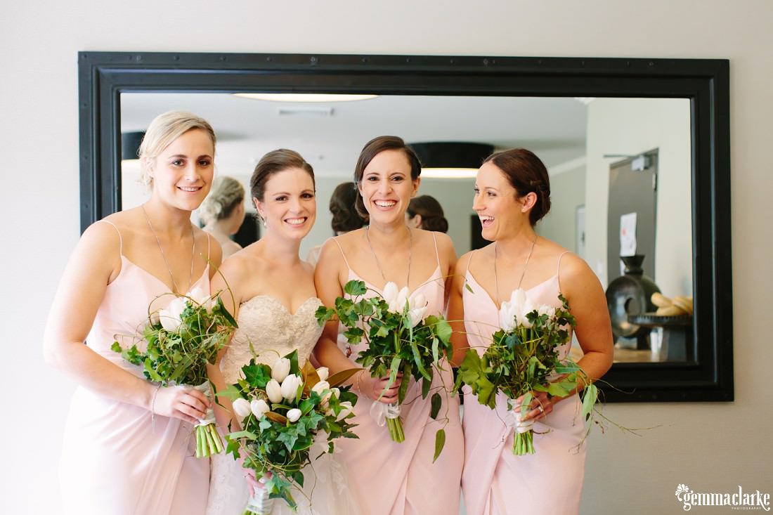 A bride and her bridesmaids smiling in front of a mirror