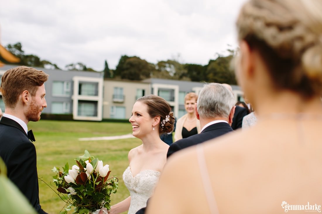 A smiling bride is given away to her groom by her father