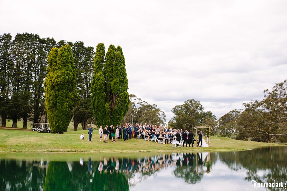 A view of the ceremony with guests and the reflection of them in the lake. Everything looks so green at this Gibraltar Hotel Wedding
