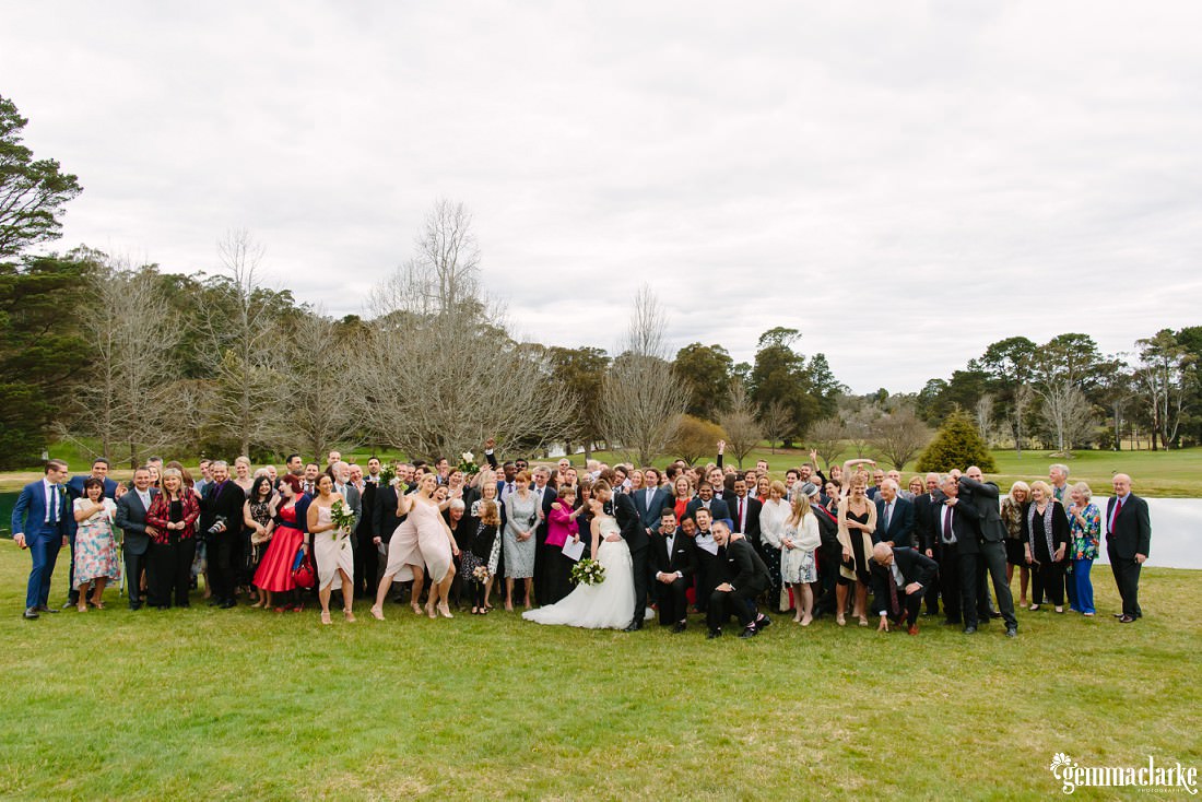 A group photo of wedding guests posing as the groom kisses his bride