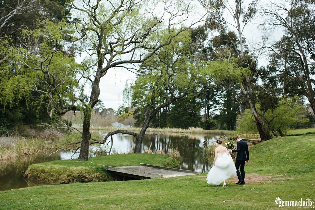 A bride and groom walking towards a small bridge to a small island in a small lake